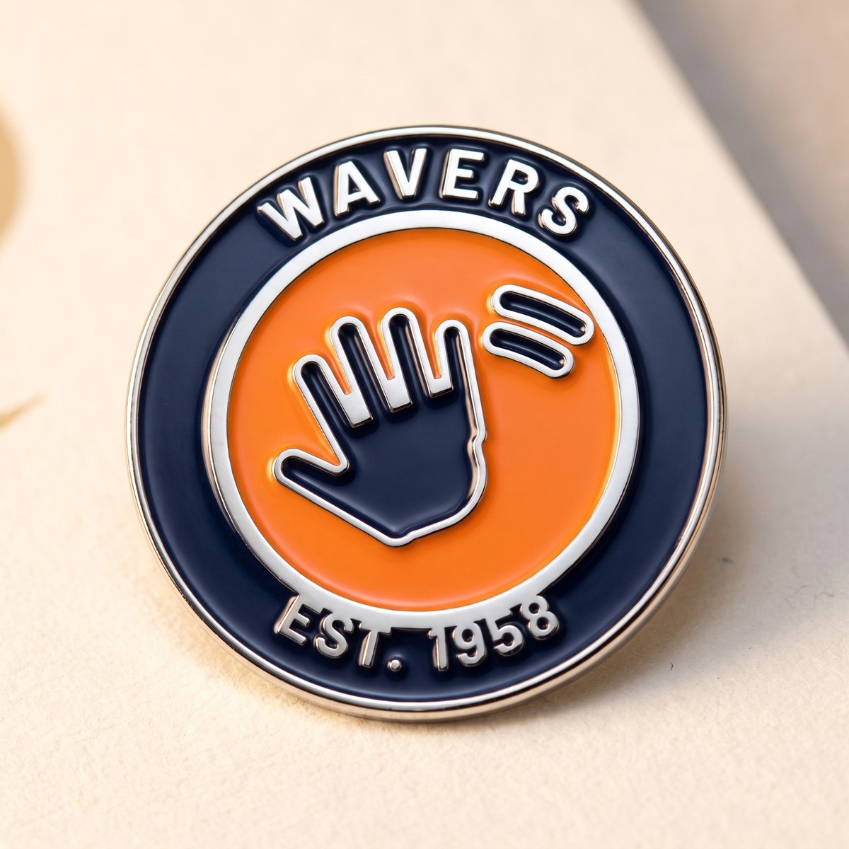 The WAVERS pin: a 25 mm hard-enamel roundel in navy and Signal Orange
